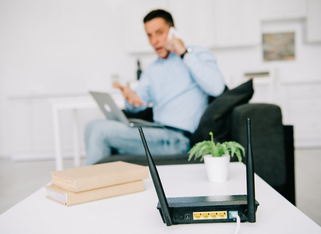 A man gestures as he gets work done with a phone, laptop and a nearby router.